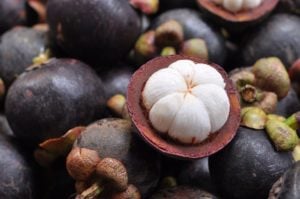 one cut mangosteen fruit on a bed of many mangosteen