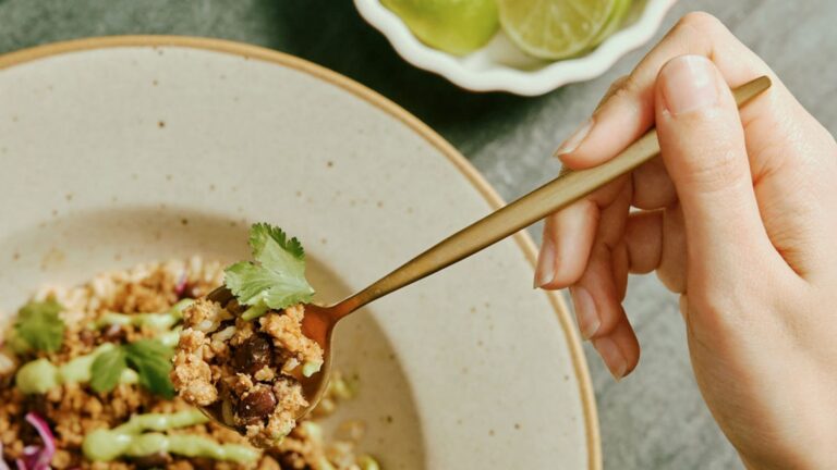 A white hand holds a spoon digging into a delicious vegan meal from Purple Carrot. The meal primarily features beans, a great source of plant based protein.