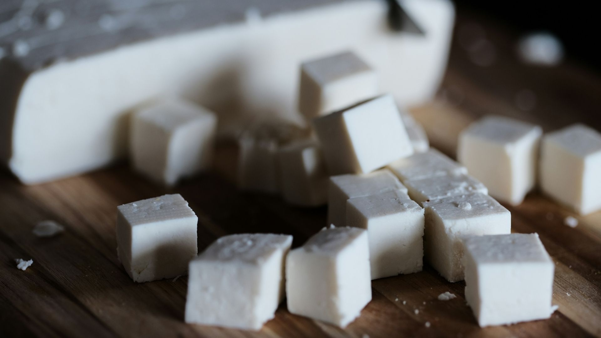 A block of tofu is cut up on a cutting board. This type of tofu is on the firmer side.