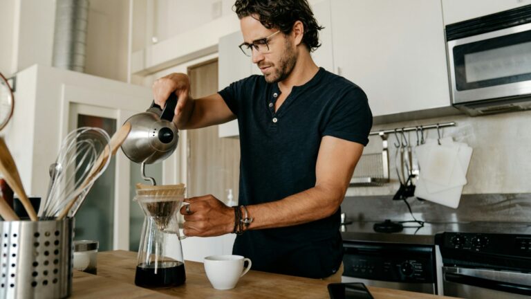 A man with dark hair and glasses stands in a kitchen making morning coffee to accompany his plant based breakfast from Purple Carrot.