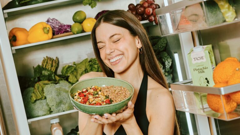 A smiling woman with dark straight hair holds a Purple Carrot meal as part of her flexitarian lifestyle.