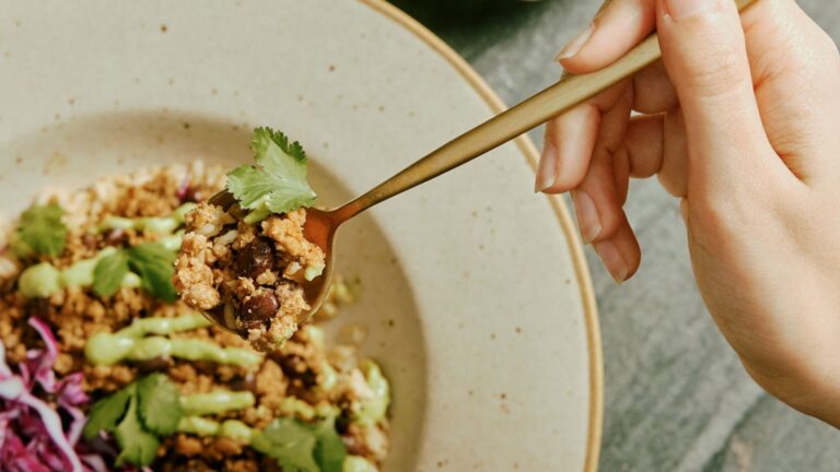 A close-up of a fork in a Purple Carrot plant-based lunch. Vibrant vegetables and grains are visible on the fork and the bowl in the background.